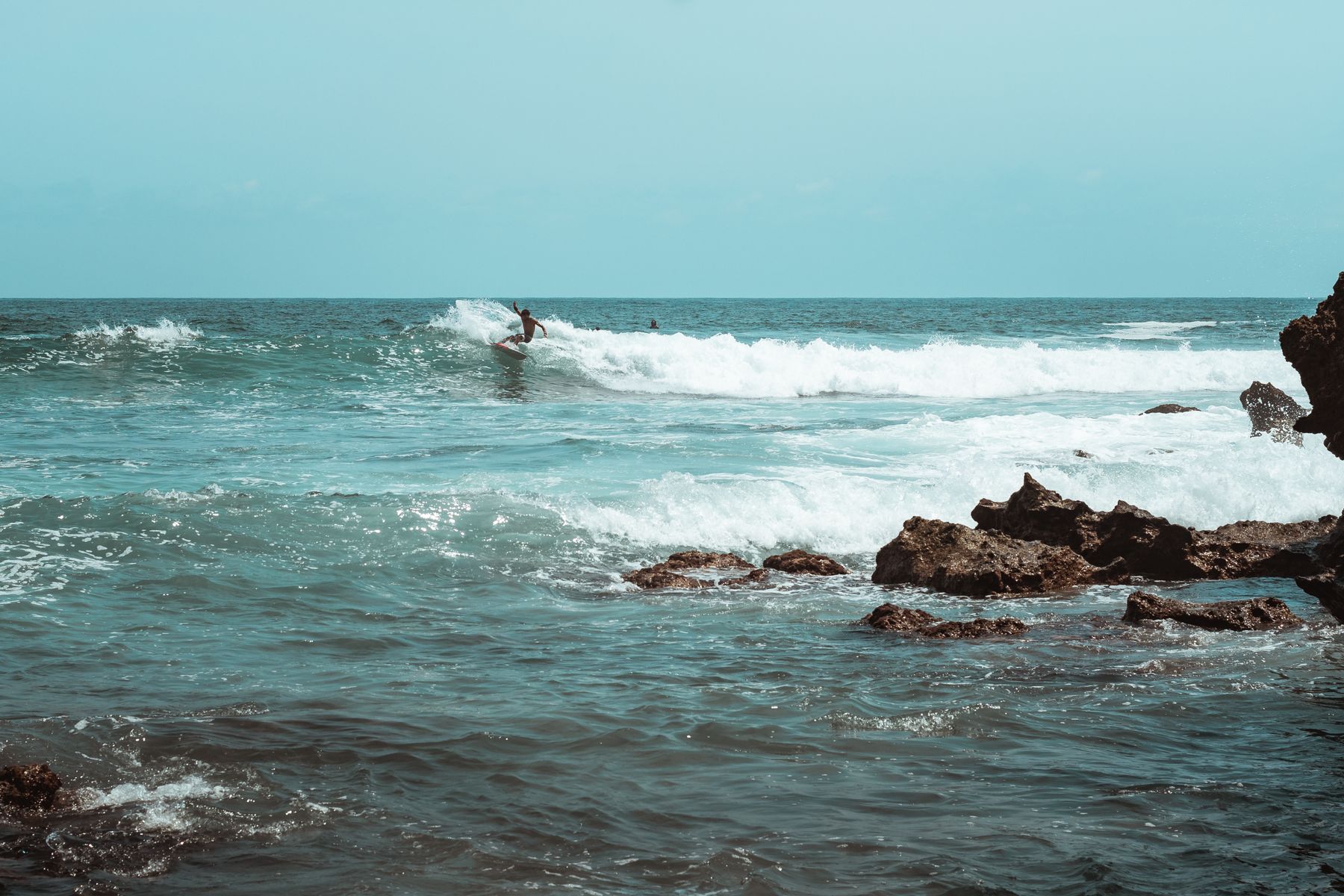 A surfer riding a wave along the rocky coastline at Puerto Escondido