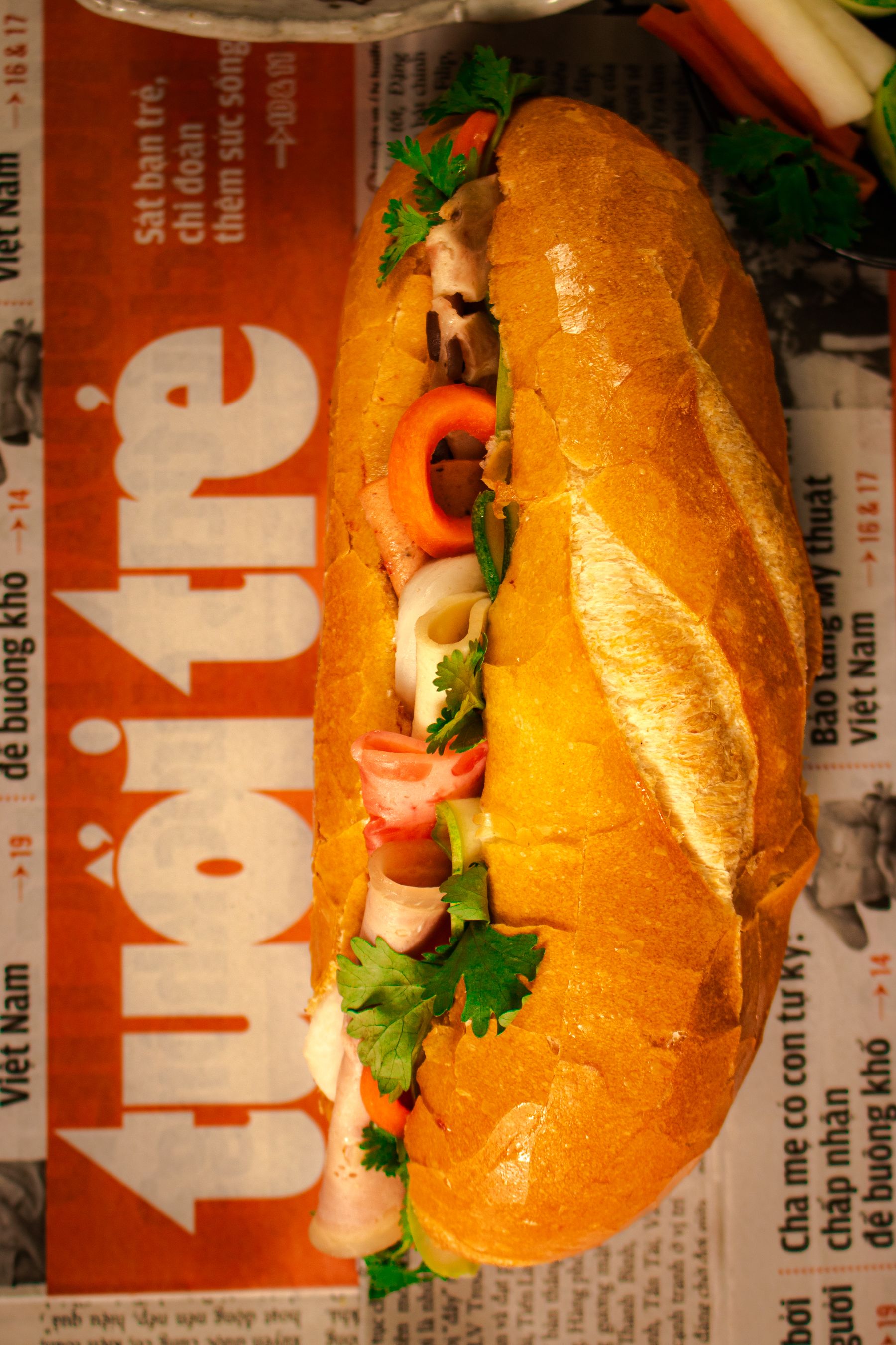 A Vietnamese banh mi sandwich filled with herbs, on newspaper