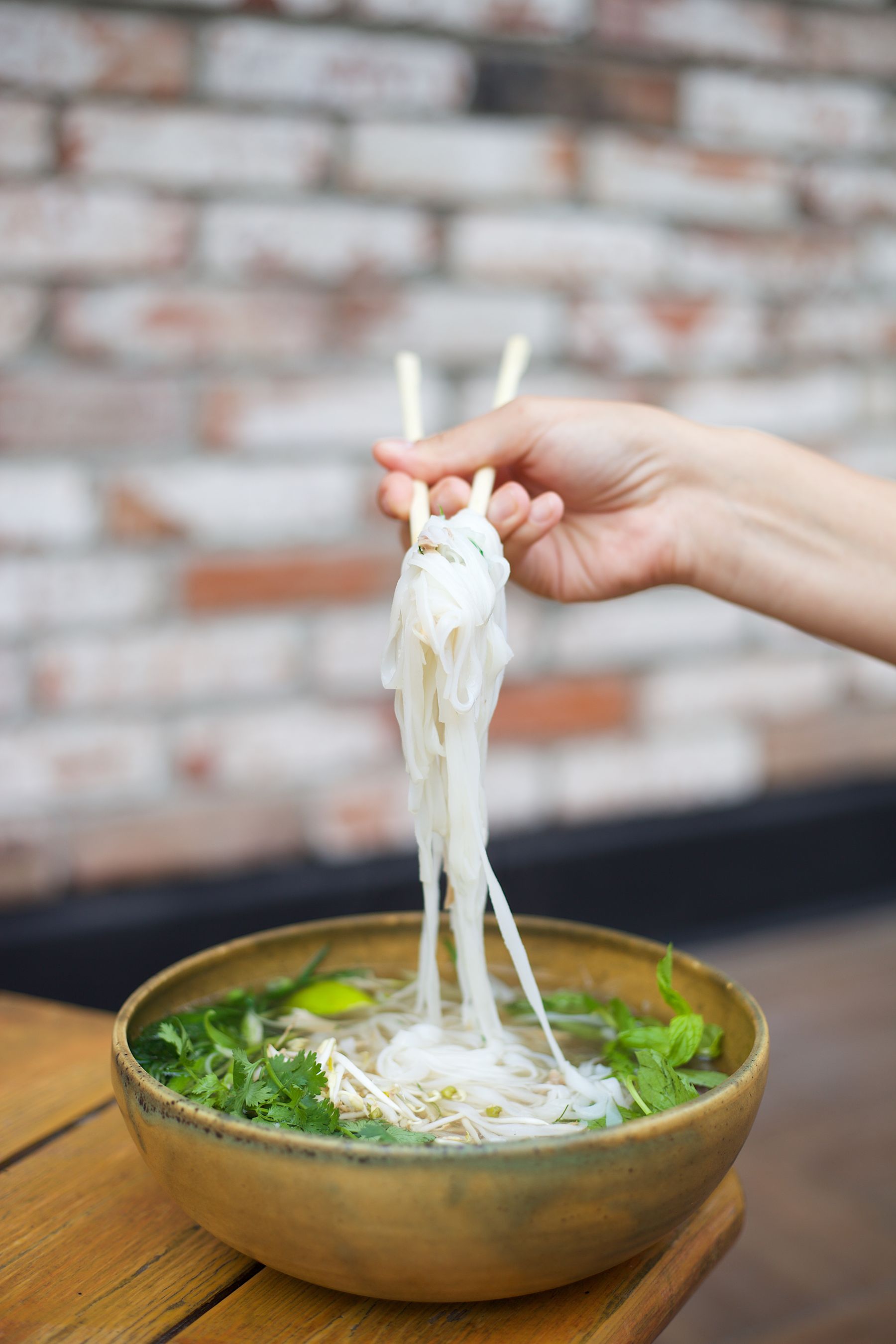 A hand lifting noodles with chopsticks from a bowl of Asian soup