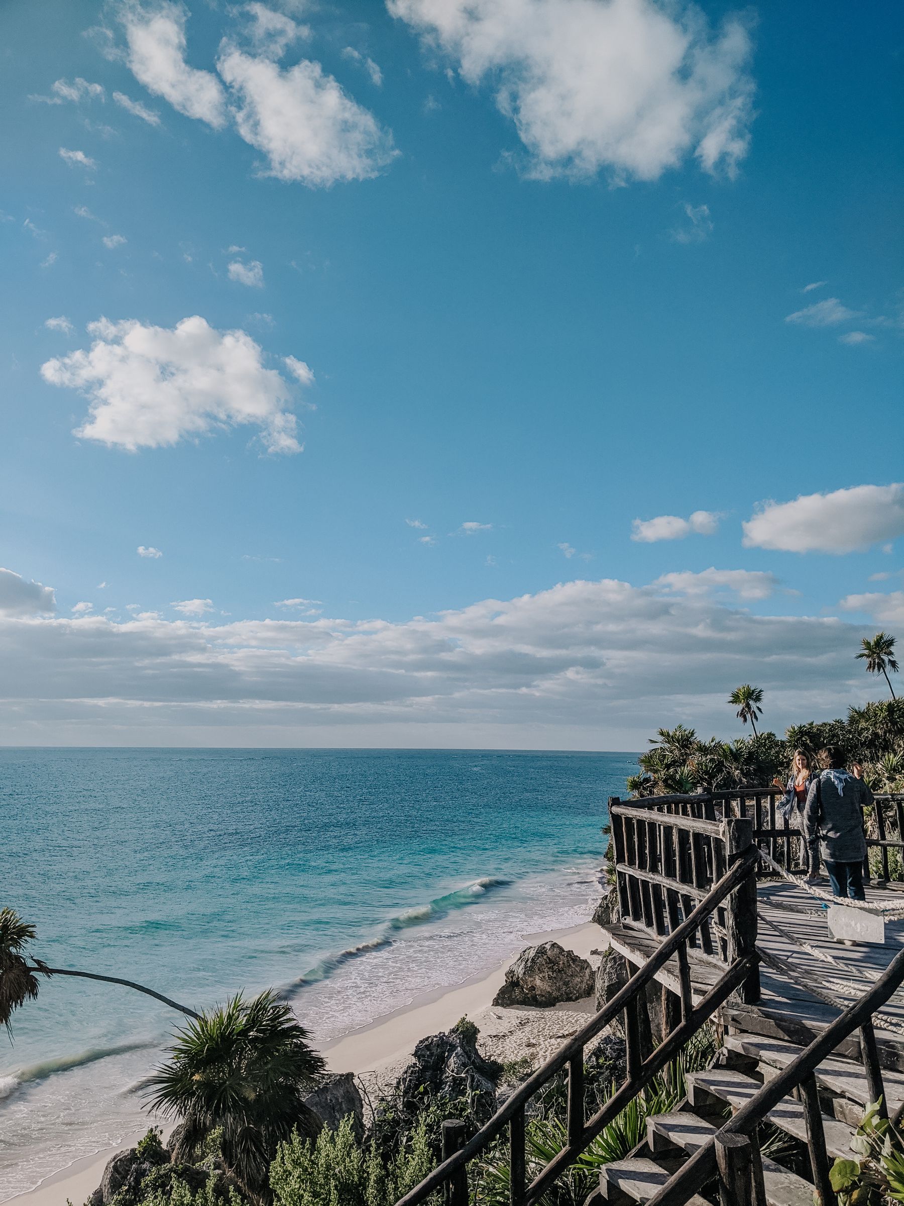 A wooden walkway leading to turquoise water and white sand in Tulum