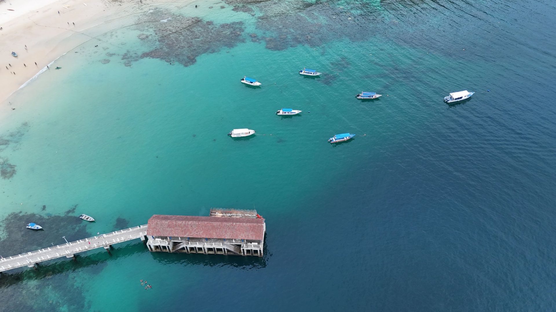 A jetty reaching into turquoise water with boats alongside