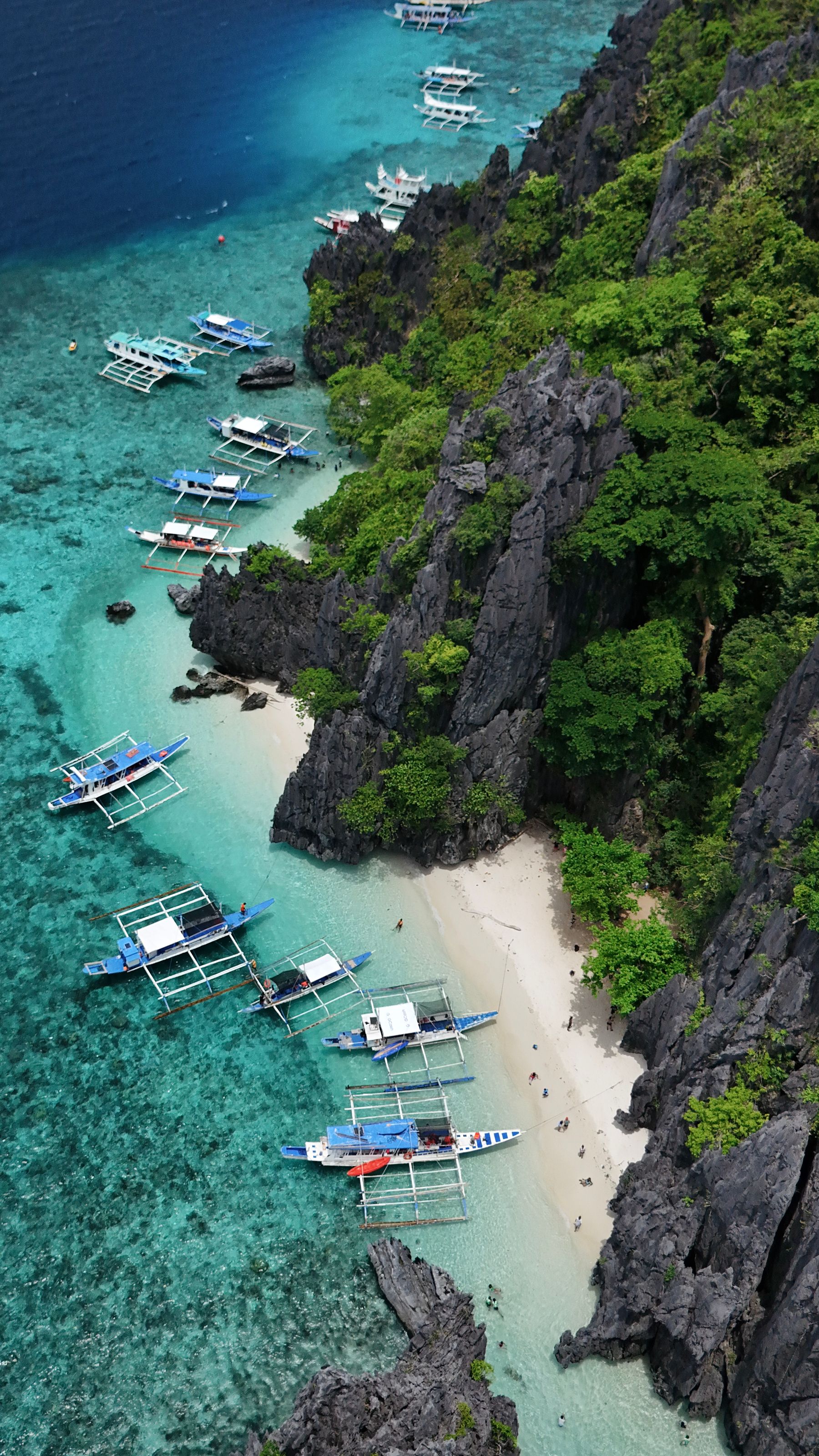 An aerial view of limestone cliffs around a turquoise lagoon