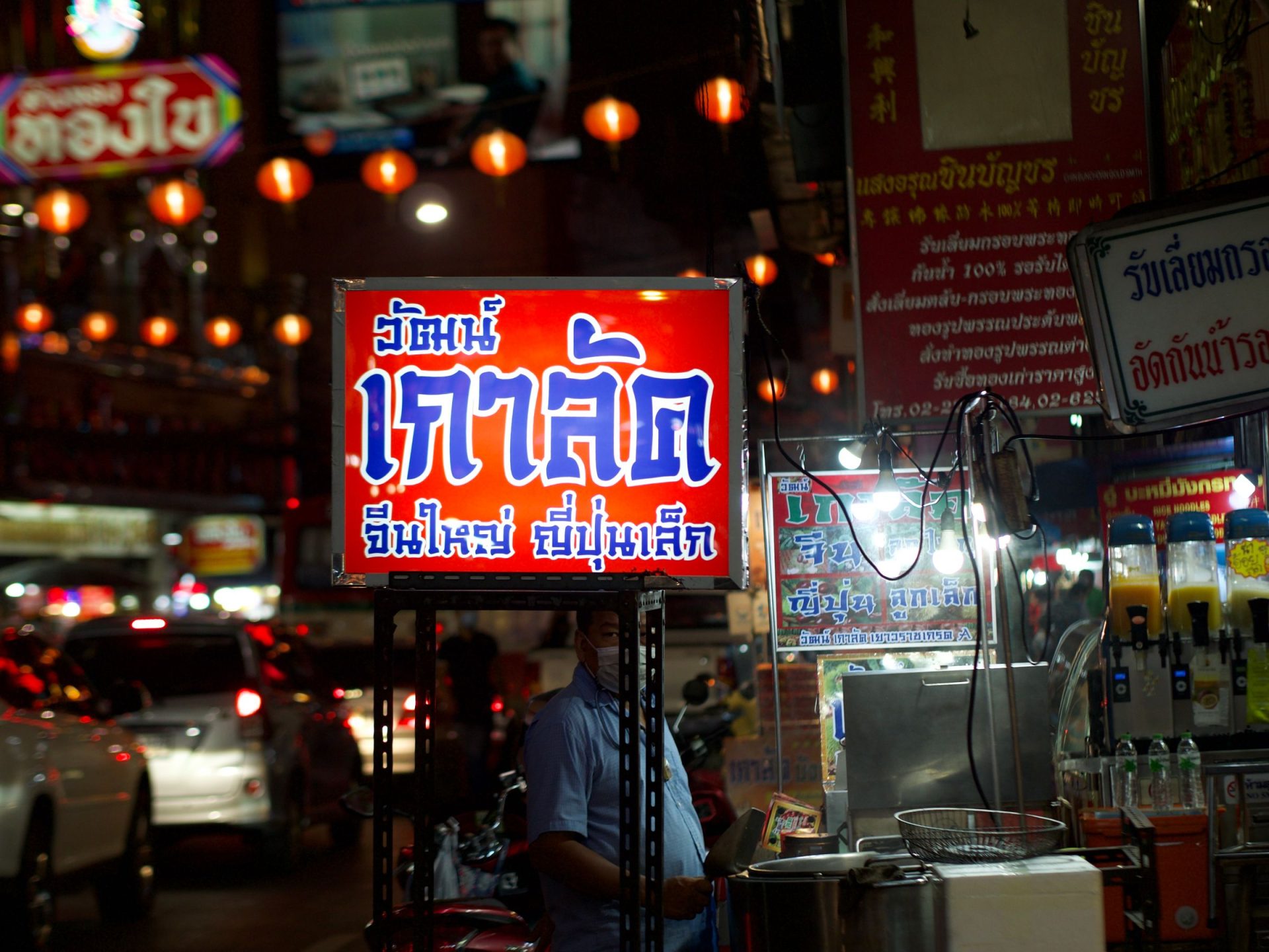 A lit Thai-script shopfront sign above a busy street at night
