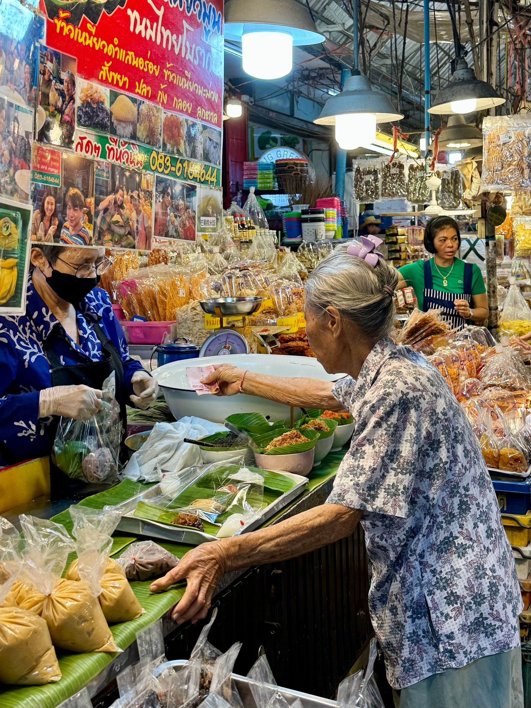 A shopper buying vegetables at a Thai market stall