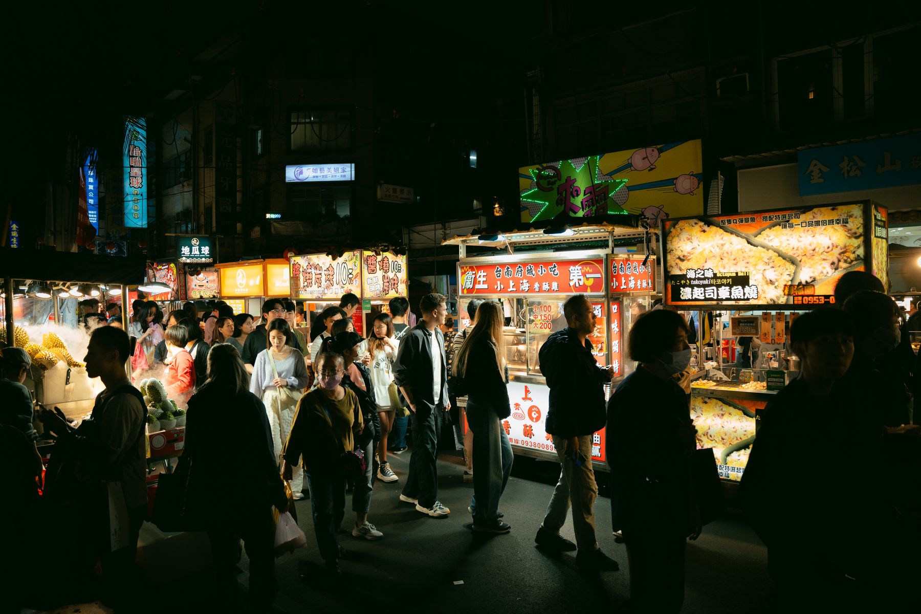 A night market filling with people between lit food stalls