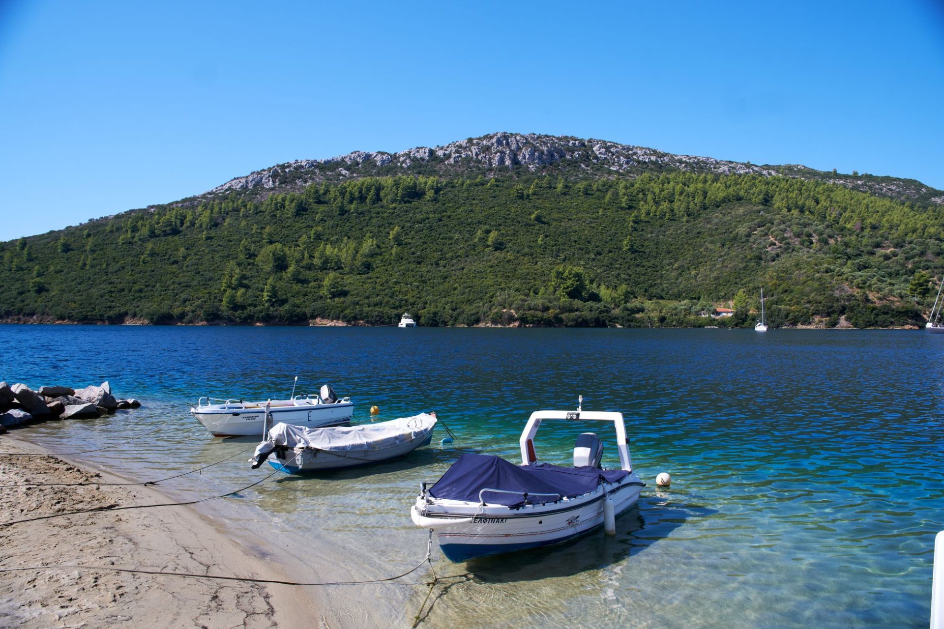 Small boats pulled up on the shore below a green headland